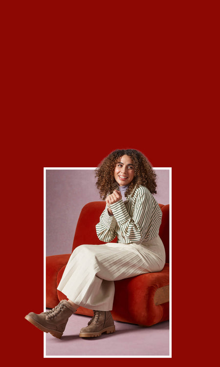 A woman sitting on a red chair in the corner, wearing a pair of Hush Puppies Aurelia Lace Boots in Taupe.